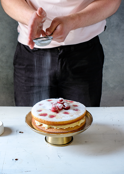 dusting Raspberry, Orange, Thyme and White Chocolate Cake with icing sugar